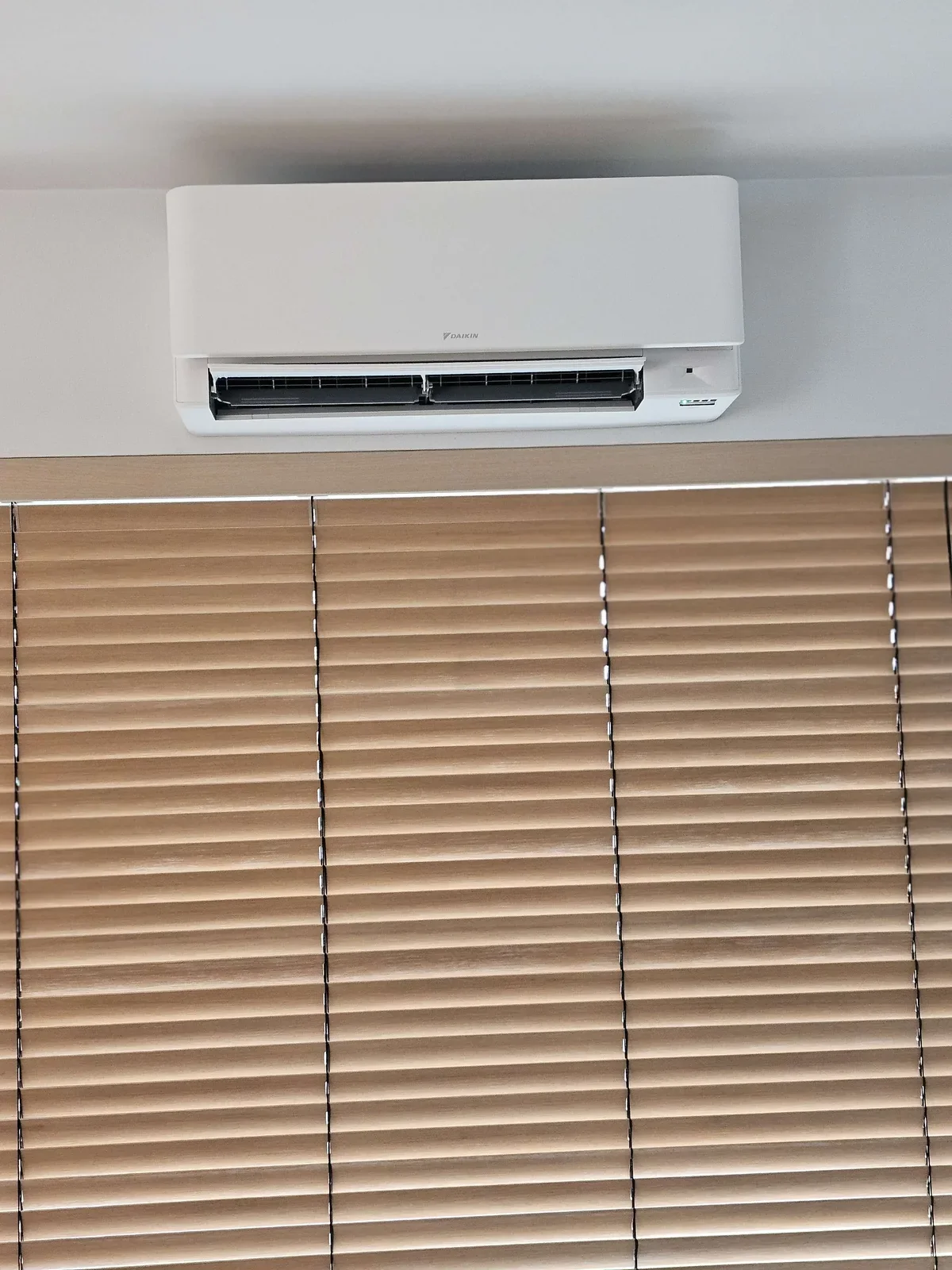 Witte airco-binnenunit boven houten jaloezieën, eigen Pattyn-installatie