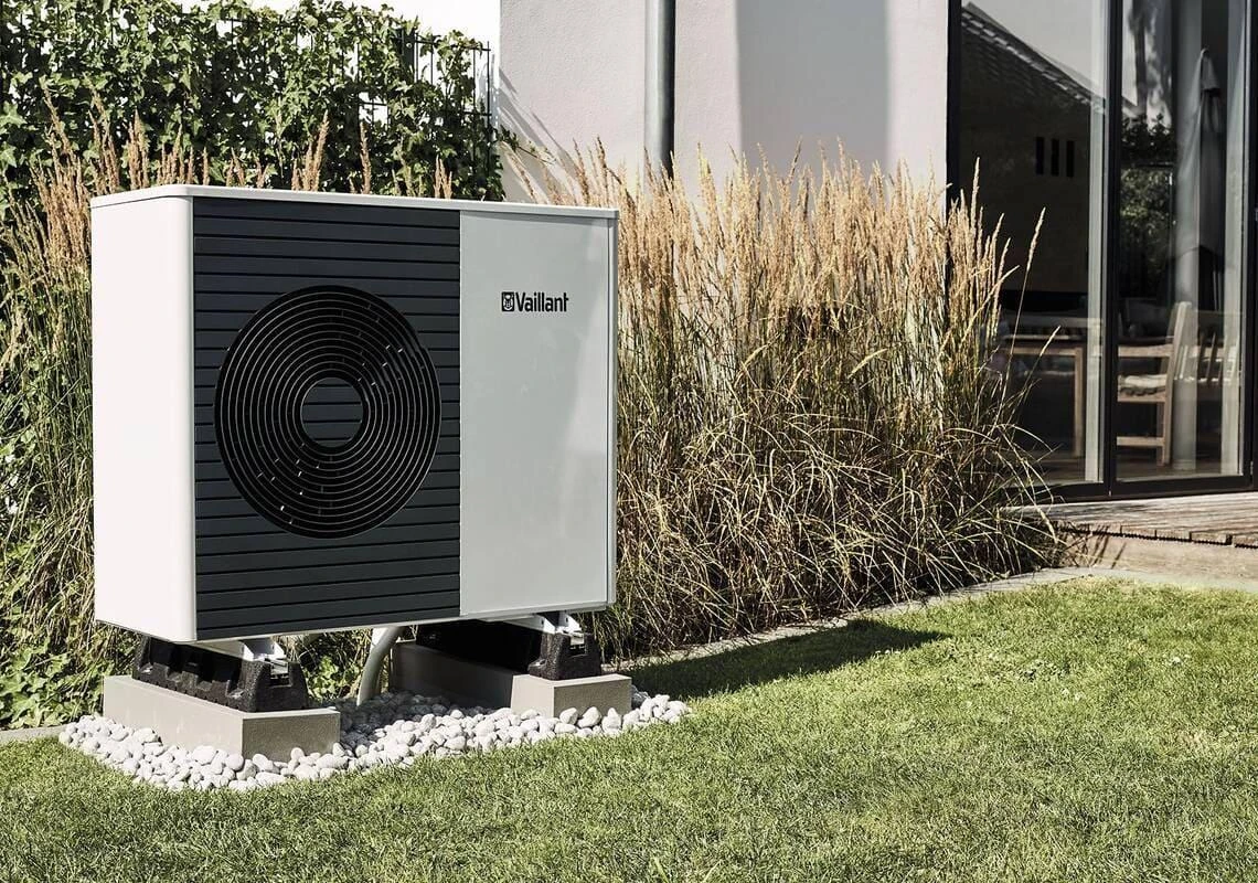 Vaillant-warmtepompbuitenunit naast siergrassen en een gazon bij een woning