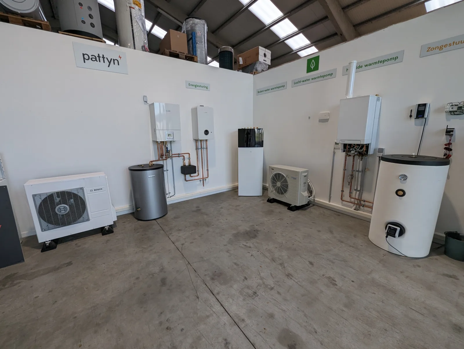 Overzicht van de Pattyn-showroom in Brugge met verschillende warmtepompen, een verwarmingsketel en warmwatertoestellen